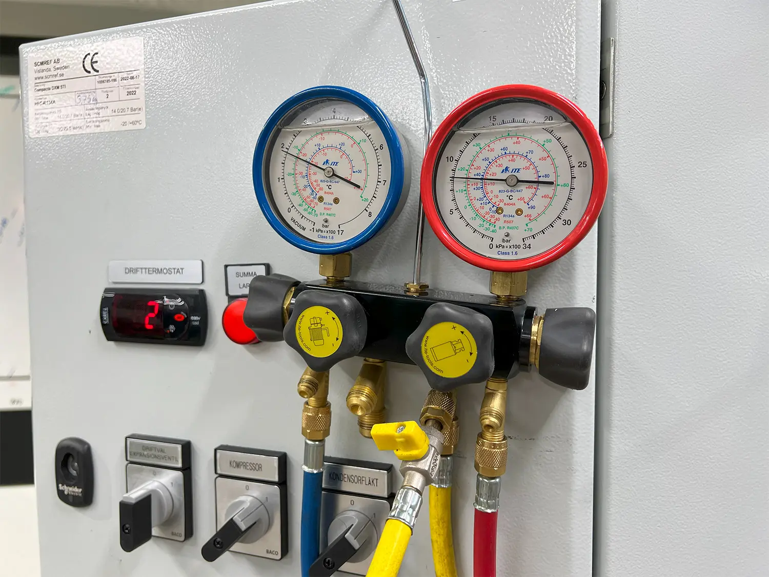 En närbild på ett manometerinstrument som mäter tryck. Det sitter fastmonterat på en panel tillsammans med andra reglage och brytare, vilket tyder på att det är en del av en utbildningsrigg inom kylteknik eller VVS – som används i en Nationell yrkesutbildning i Eskilstuna.