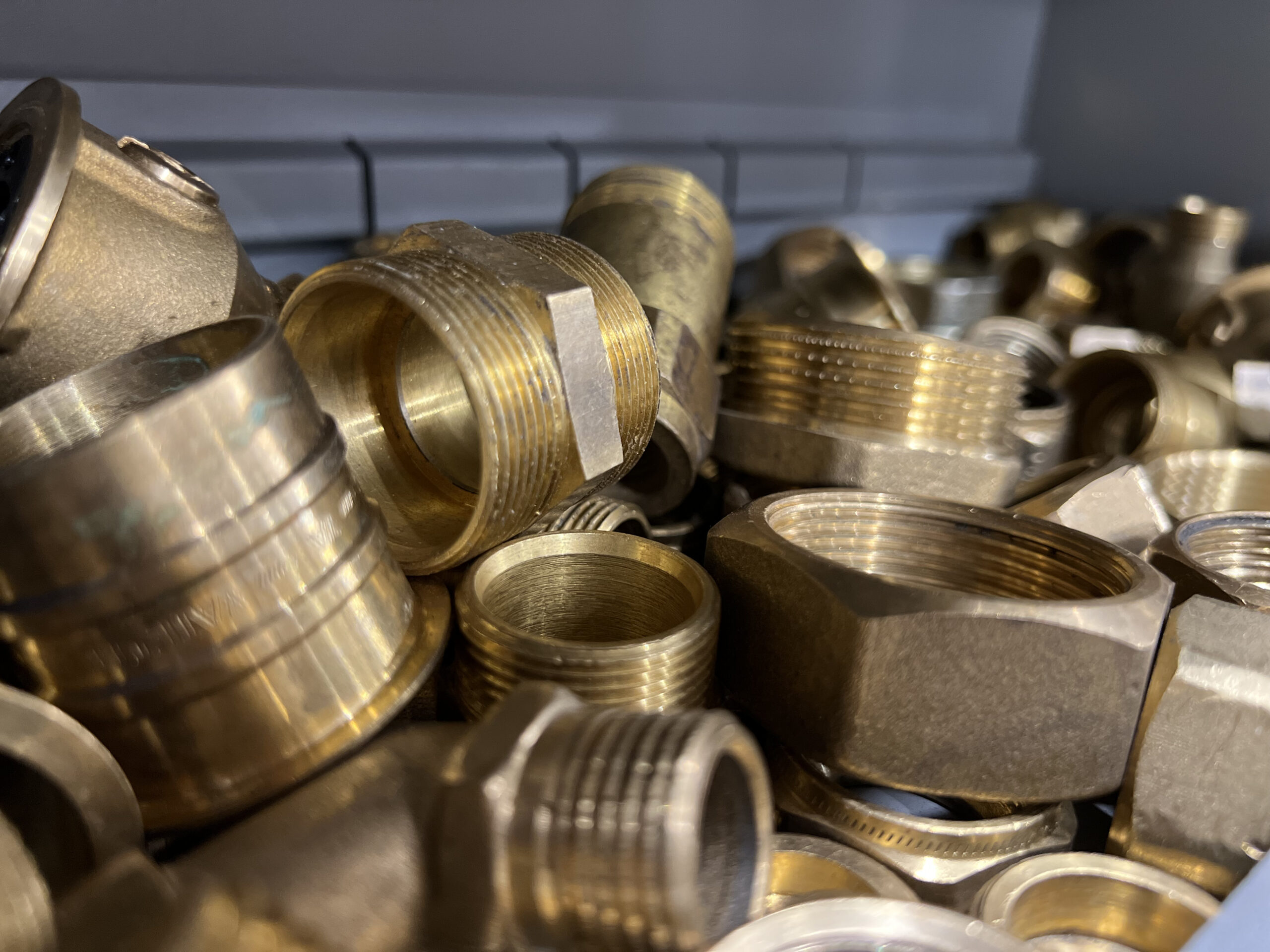 Närbild på ett fack med metallkopplingar och rördelar i mässing – detaljer som används inom VVS-området. Bilden är tagen i en verkstadsmiljö som tillhör en arbetsmarknadsutbildning i Göteborg hos Movant. Fokus på material och precision speglar den praktiska delen av utbildningen, där deltagarna får arbeta med verklighetsnära moment och utveckla yrkeskunskaper efter branschens behov.