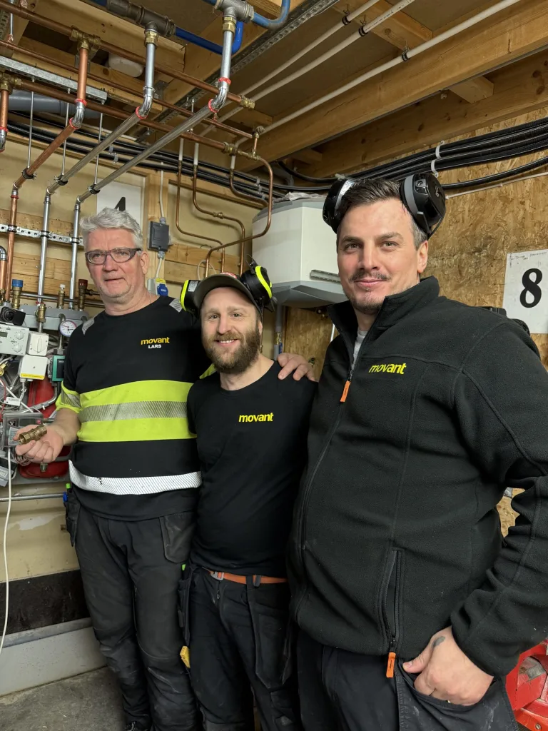 Tre män i arbetsmarknadsutbildning i Halmstad står i en teknisk miljö hos Movant, omgivna av rör och ventiler. De ser samarbetsvilliga och fokuserade ut.