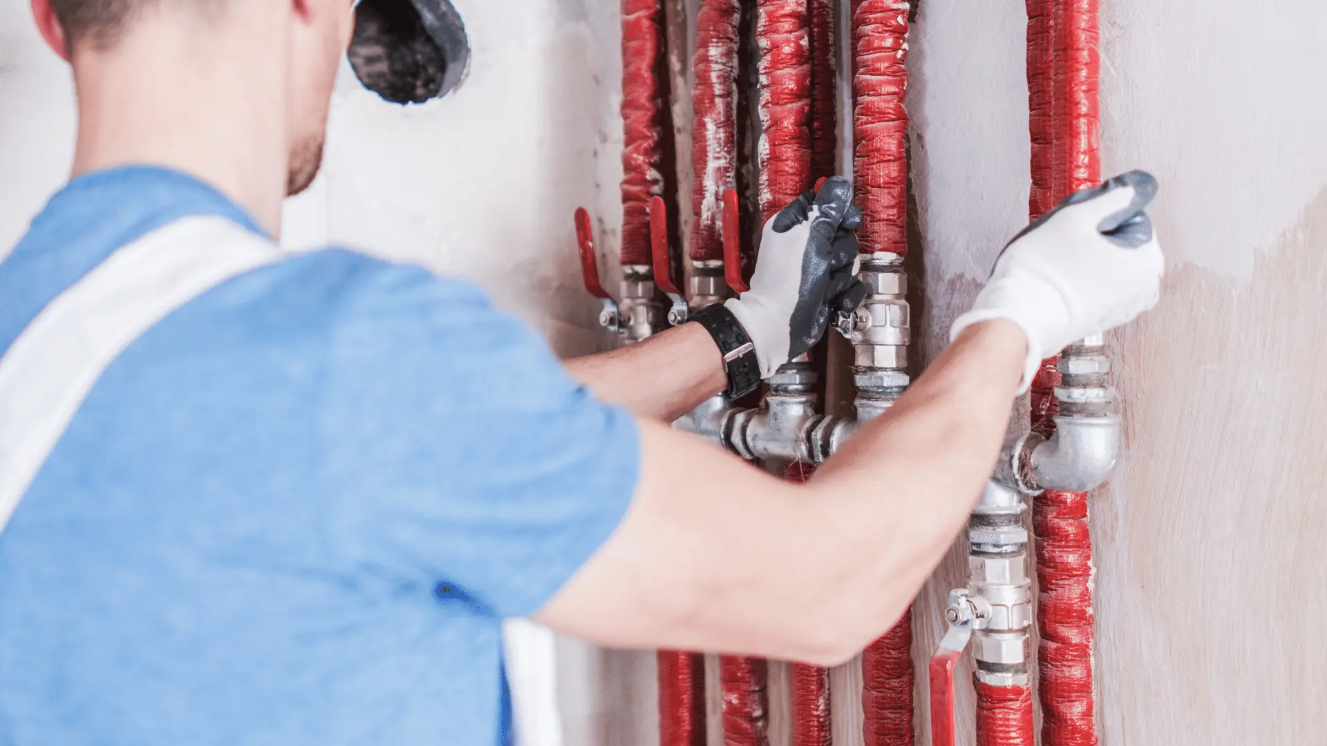 En ventilationstekniker i arbete justerar isolerade rör och ventiler längs en vägg. Teknikern bär skyddshandskar och arbetar noggrant med installation eller underhåll av ett ventilationssystem.