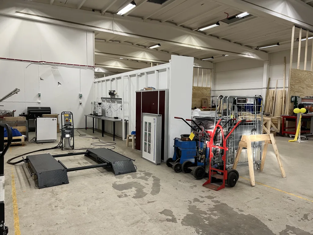 Öppen verkstadsyta med lyftplattform, gasutrustning på vagnar och olika tekniska stationer uppställda längs väggarna.