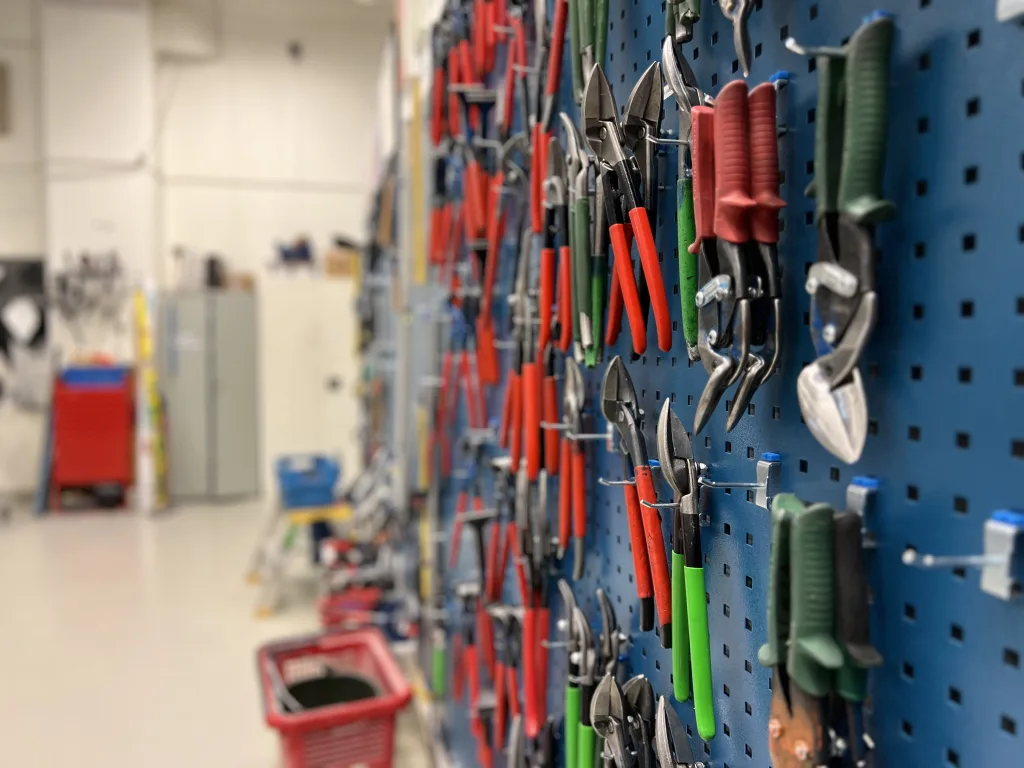 Närbild på vägg med upphängda plåtsaxar och tänger i olika färger i en organiserad verkstadsdel.