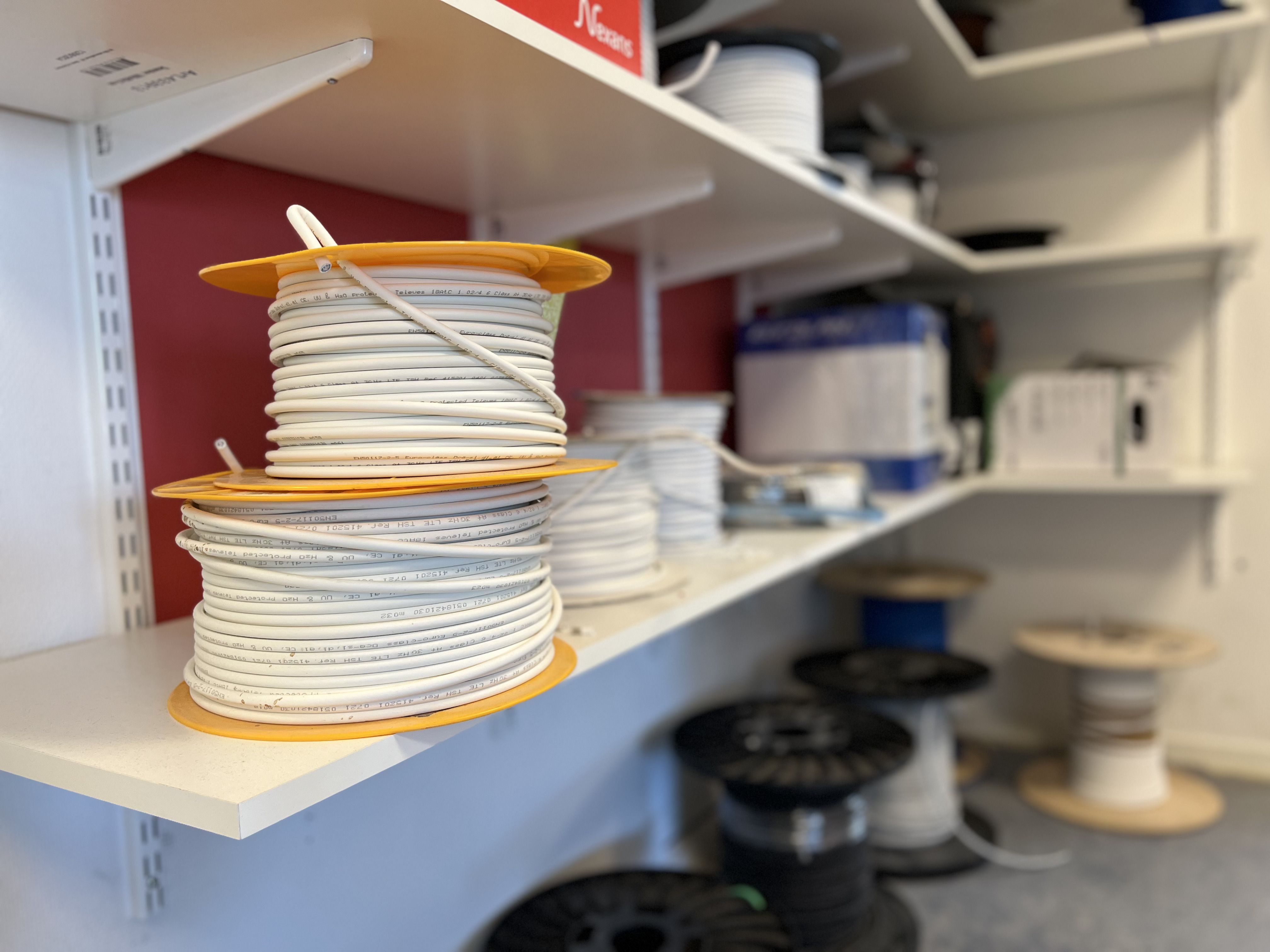 Hyllor med kabelrullar i olika färger och storlekar på movant i uppsala. Förgrunden visar två rullar med vit elkabel och bakgrunden innehåller fler kablar och elmaterial.