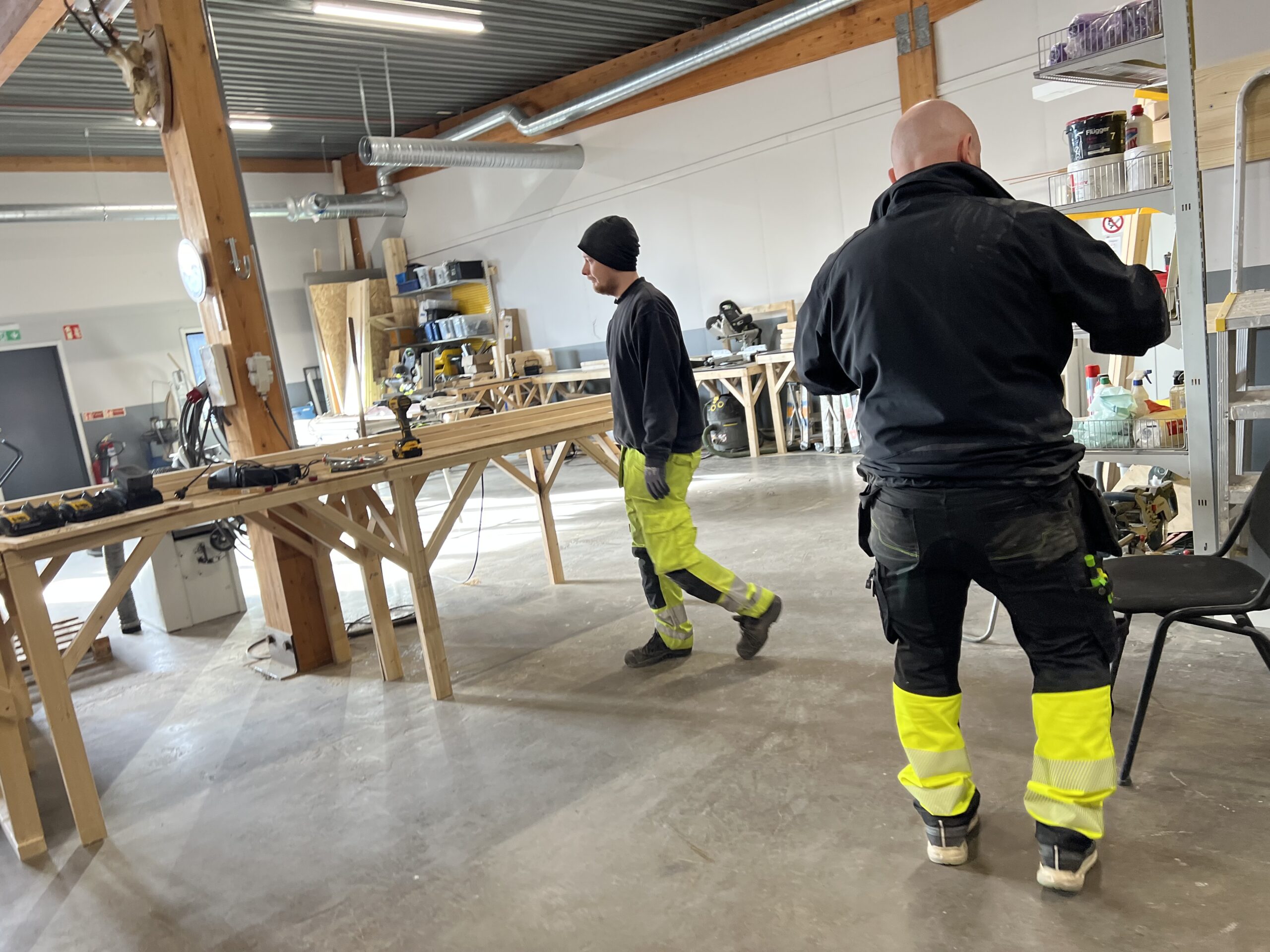 Två personer i arbete vid träbänkar i Movant Varbergs bygglokaler med verktyg i fokus.