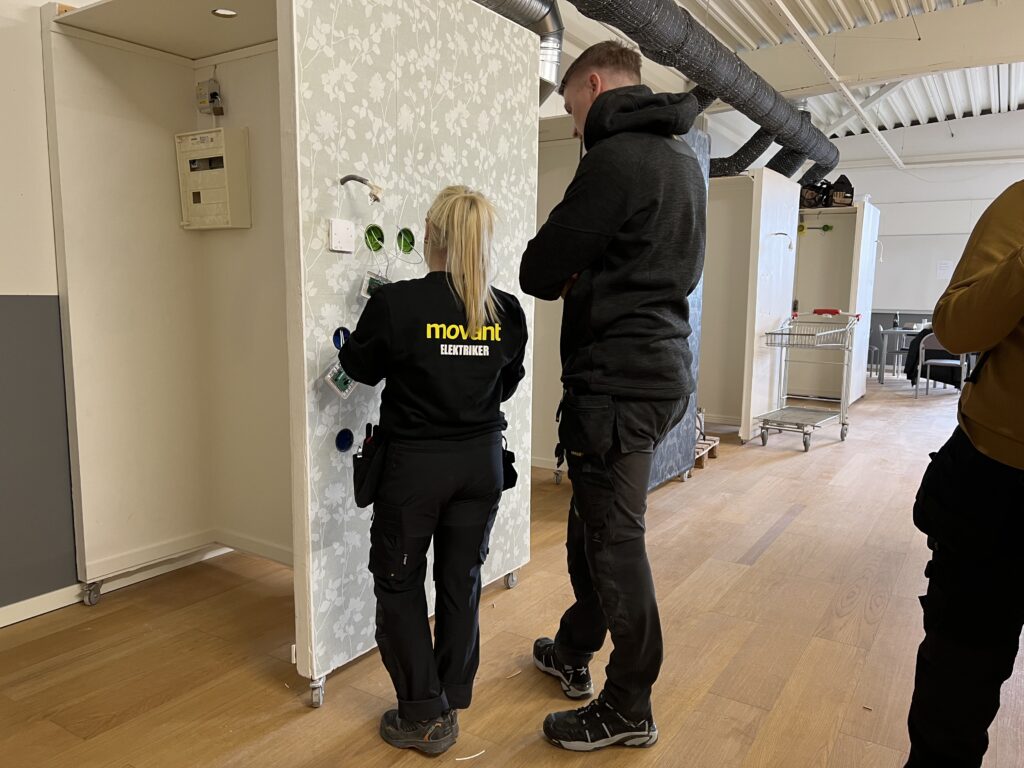 Elev från Movant Varberg installerar elkomponenter på en övningsvägg tillsammans med handledare.