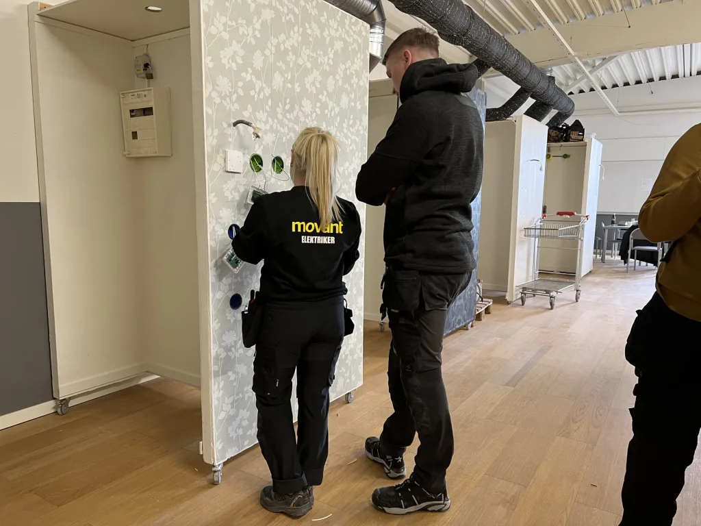 Elev från Movant Varberg installerar elkomponenter på en övningsvägg tillsammans med handledare.
