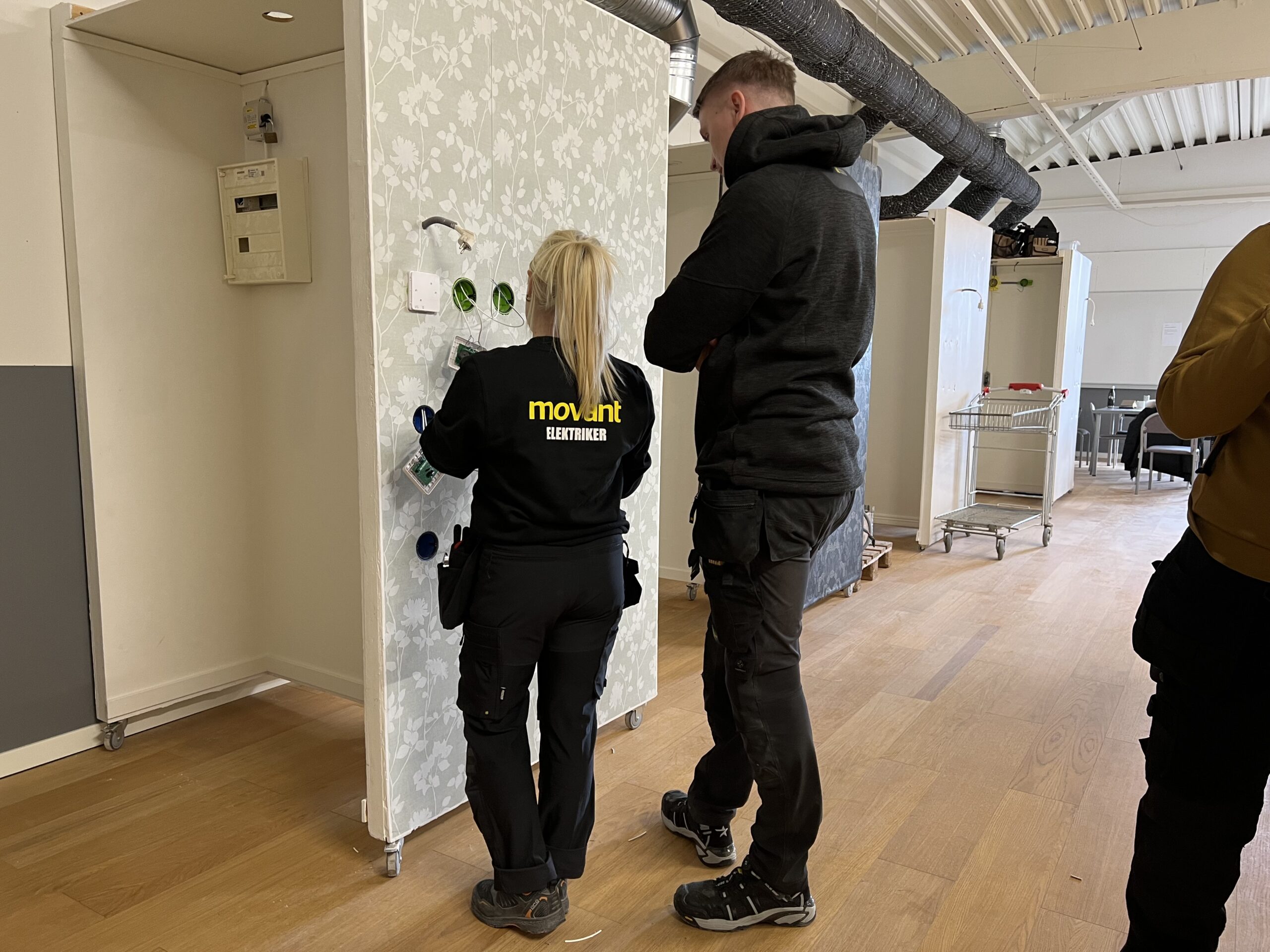 Elev från Movant Varberg installerar elkomponenter på en övningsvägg tillsammans med handledare.
