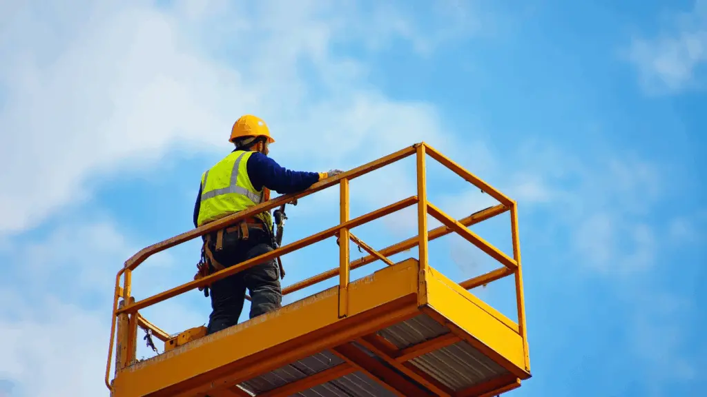En arbetare i hjälm och reflexväst står på en upphöjd liftplattform mot en klar himmel och utför arbete på höjd. Bilden betonar säkerhet, balans och korrekt användning av utrustning inom liftutbildning i praktisk arbetsmiljö. Denna bild är skapad med hjälp av AI.