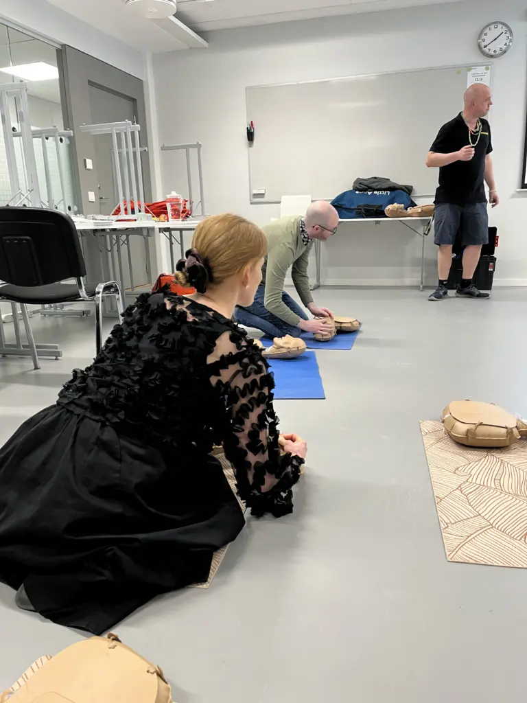 Deltagare följer en instruktör under en HLR-utbildning hos Movant och tränar bröstkompressioner på övningsdockor. Utbildningen sker i ett klassrum med fokus på praktiska moment och handledning i realtid.